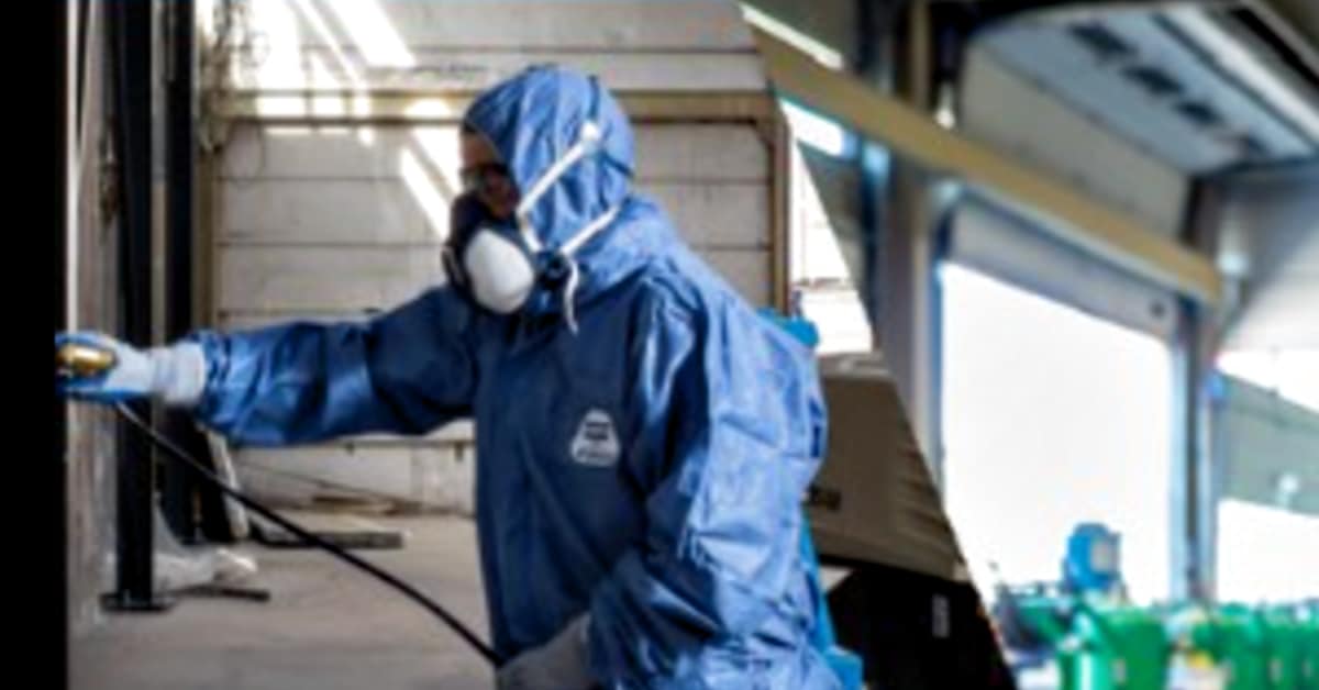 peintre portant un équipement de protection individuelle et utilisant un pulvérisateur sans air