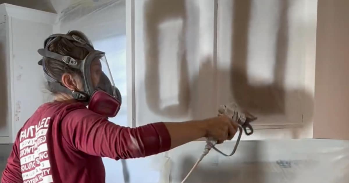 person using airless paint sprayer to paint cabinets